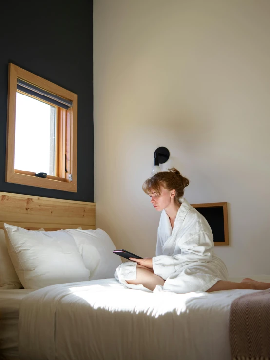 a woman sitting on a bed reading a book, passive house, hotel room, profile image, in a cabin