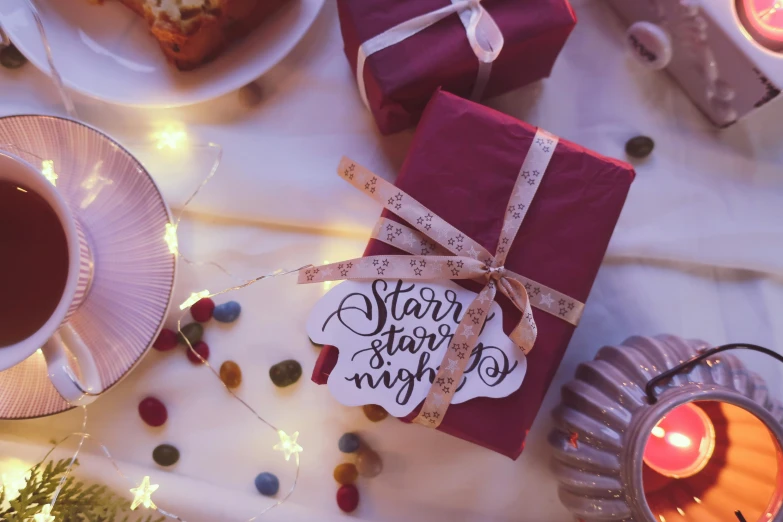 a table topped with plates of food and a cup of tea, by Alice Mason, pexels contest winner, graffiti, birthday wrapped presents, maroon, fairy lights, starlight