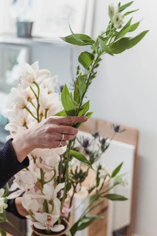 a woman arranging flowers in a vase on a table, trending on unsplash, magnolia big leaves and stems, detail shot, large tall, dynamic angled shot