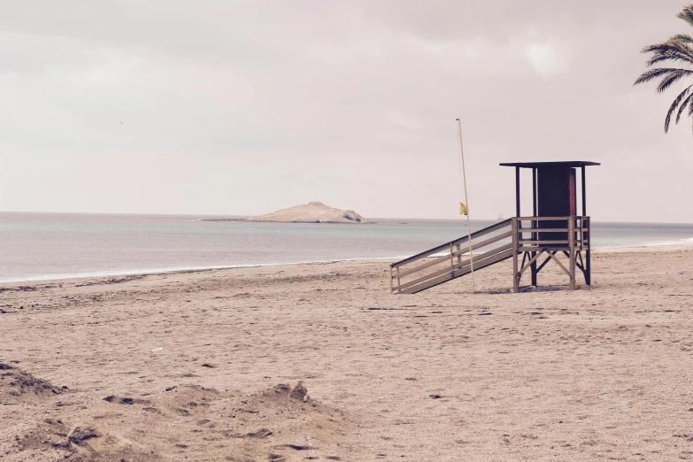 a lifeguard tower sitting on top of a sandy beach, a photo, by Caro Niederer, unsplash, minimalism, muted brown, costa blanca, huts, grey skies