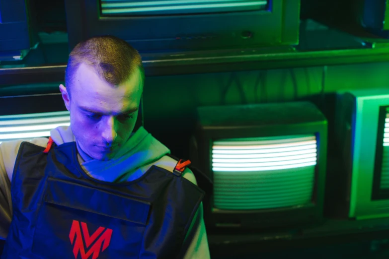 a man sitting in front of a bunch of televisions, an album cover, by Adam Marczyński, unsplash, graffiti, model is wearing techtical vest, red and blue back light, military vest, mr beast