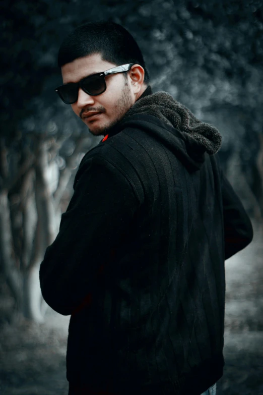 a man standing in the middle of a forest, an album cover, inspired by Rudy Siswanto, pexels contest winner, realism, wearing shades, wearing a black sweater, headshot profile picture, hacker