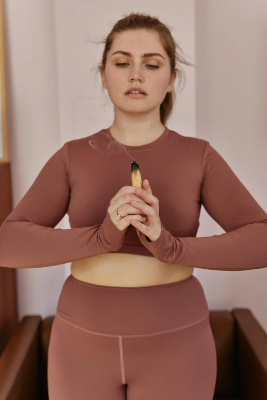 a woman holding a banana in her hands, a digital rendering, inspired by Louisa Matthíasdóttir, trending on pexels, cropped red yoga short, incense, long sleeve, terracotta