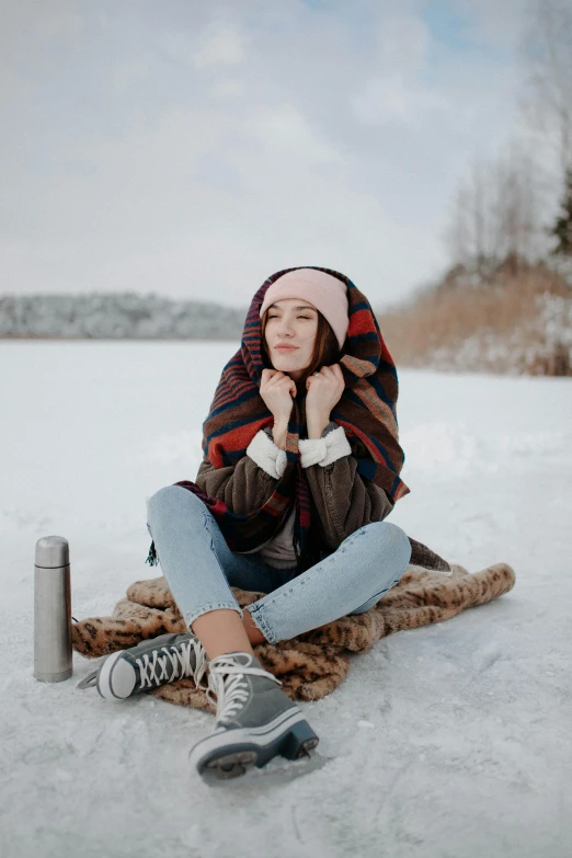 a woman sitting on a blanket in the snow, trending on pexels, russian clothes, polish hyper - casual, frozen lake, beanie