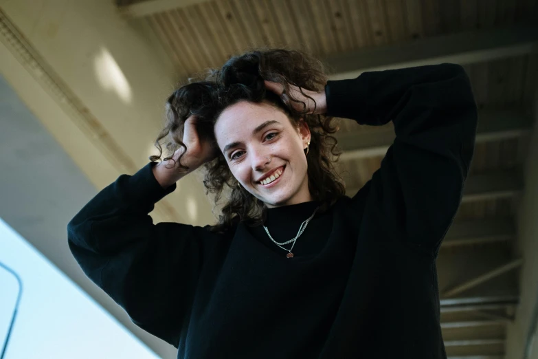 a woman standing in front of a laptop computer, a photo, by Niko Henrichon, pexels contest winner, wearing a black sweater, curls, portrait androgynous girl, smiling down from above