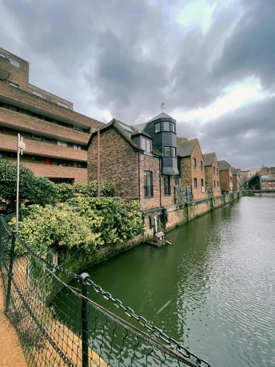 a large body of water next to a building, by IAN SPRIGGS, railing along the canal, on a cloudy day, high res 8k, multiple stories