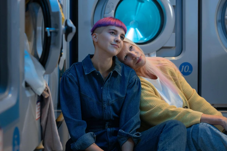 two women sitting next to each other in front of a washing machine, trending on pexels, cyberpunk dyed haircut, scene from live action movie, lesbian embrace, stålenhag