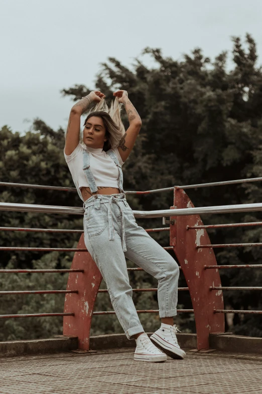 a woman posing for a picture on a bridge, trending on pexels, baggy pants, wearing off - white style, she is dancing, desaturated