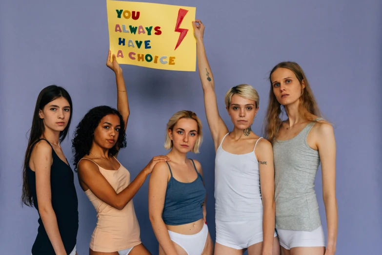 a group of women standing next to each other holding a sign, a photo, trending on pexels, feminist art, wearing a camisole and shorts, bisexual lighting, profile image, anorexic figure