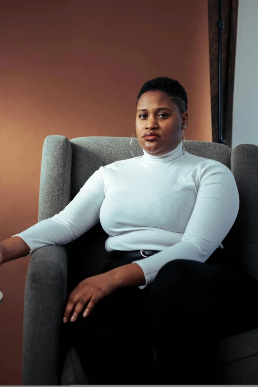 a woman sitting in a chair in a room, by Lily Delissa Joseph, in white turtleneck shirt, plus-sized, non-binary, 2019 trending photo