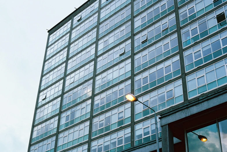 a tall building with a street light in front of it, inspired by Richard Wilson, bauhaus, cyan shutters on windows, glasgow, exterior shot, floor - to - ceiling windows