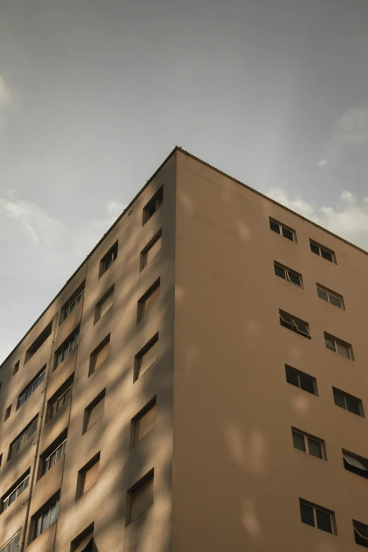 a tall tan building with lots of windows, inspired by André Kertész, unsplash, light and shadow, a ghetto in germany, low quality photo, cinematic view from lower angle