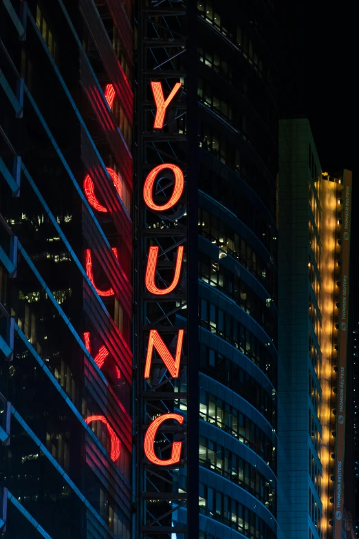 a large neon sign on the side of a tall building, neil young design, city lights, youth, dynamic closeup