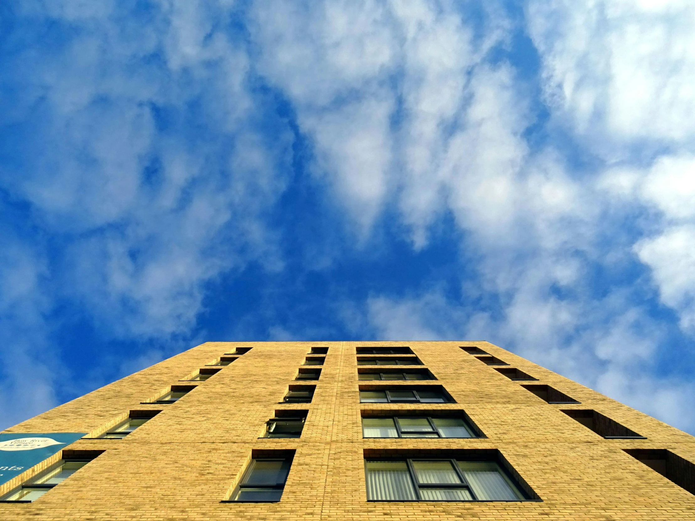 a tall brick building with a blue sky in the background, by Washington Allston, unsplash, brutalism, high clouds, ten flats, 2 0 0 0's photo, golden windows