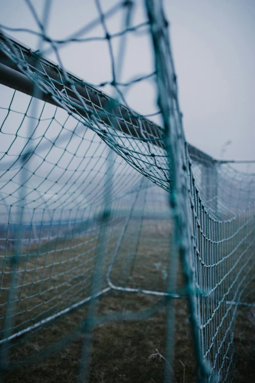 a close up of a fence with a field in the background, inspired by Elsa Bleda, unsplash, conceptual art, football, grey, mesh structure, battered