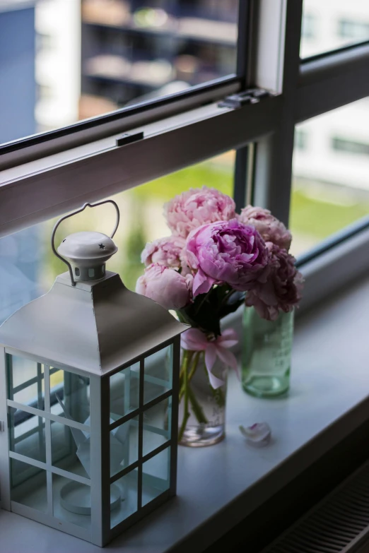 a lantern sitting on a window sill next to a vase of flowers, pink flowers, peony flowers, city views, indoor picture