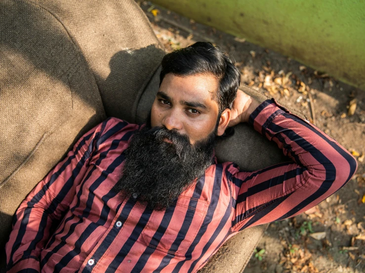 a man with a long beard laying on a couch, pexels contest winner, hurufiyya, assamese, wearing a flannel shirt, retro stylised, **cinematic