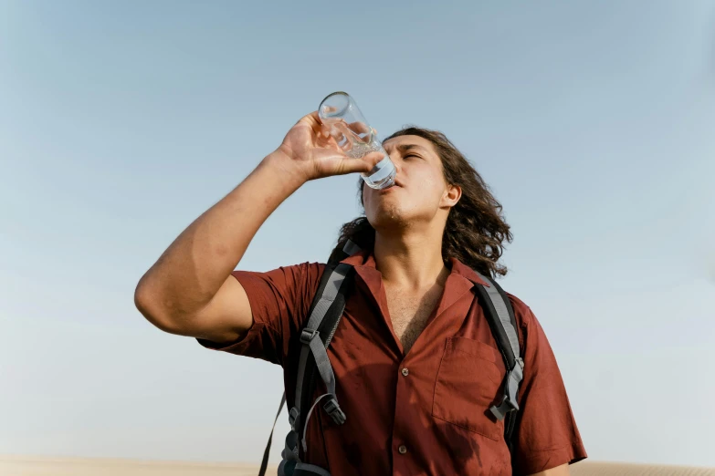 a man in a red shirt drinking from a water bottle, pexels contest winner, renaissance, in the australian desert, avatar image, middle eastern skin, avan jogia angel