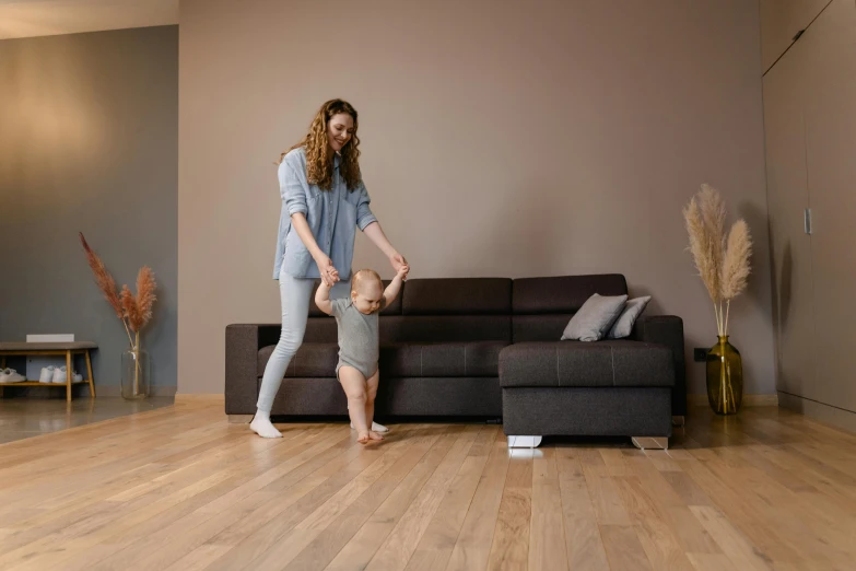 a woman standing next to a baby in a living room, pexels contest winner, minimalism, she is dancing. realistic, wooden floors, sofa, low quality photo