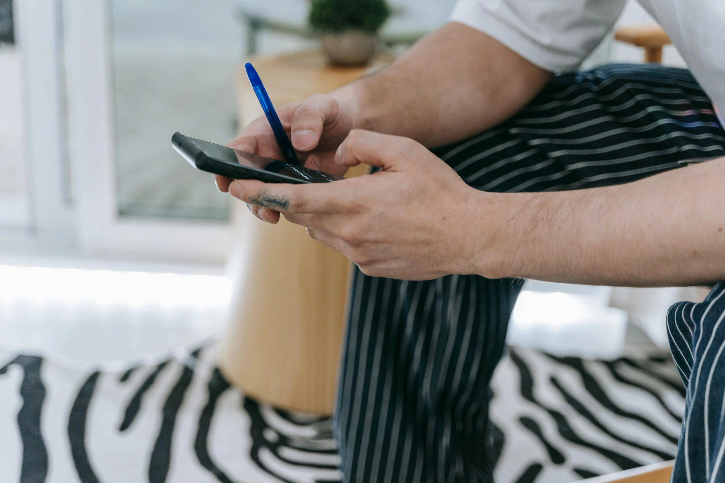 a close up of a person holding a cell phone, a cartoon, trending on pexels, arbeitsrat für kunst, stripey pants, sitting across the room, blue ballpoint pen, penned with black on white