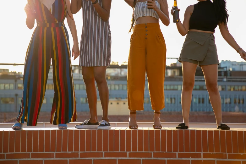 a group of women standing on top of a brick wall, trending on pexels, rooftop party, on a yellow canva, pants, in spain