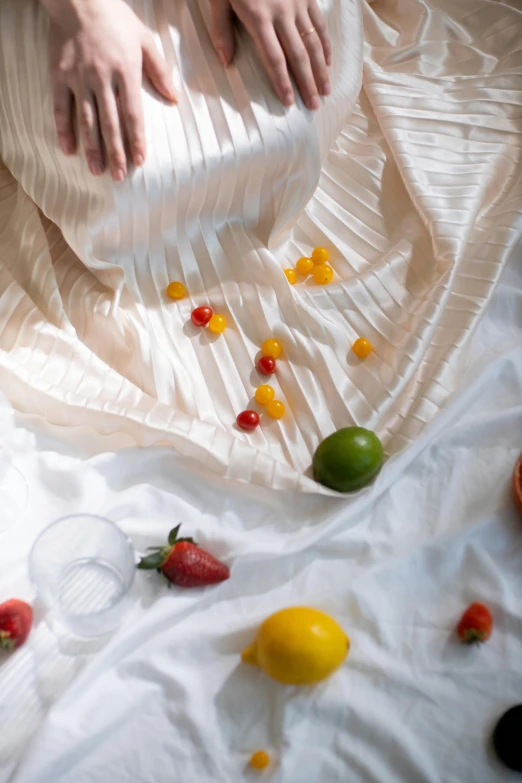 a woman sitting on top of a bed covered in fruit, inspired by Wilhelm Hammershøi, unsplash, coated pleats, drinks, close up details, tablecloth