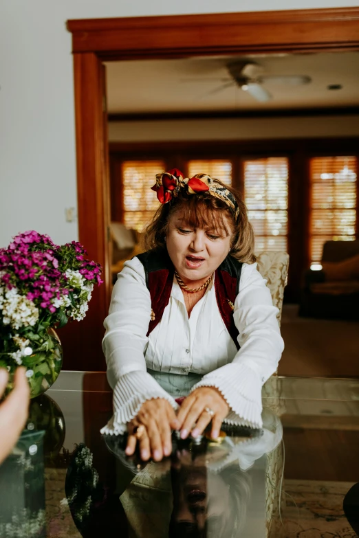 a woman sitting at a table with a vase of flowers, playing games, cottage hippie naturalist, wearing a headband, non blurry