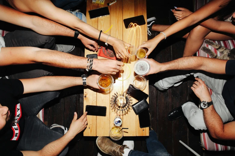 a group of people sitting around a wooden table, by Niko Henrichon, pexels, holding a drink, lit from above, snapchat photo, college