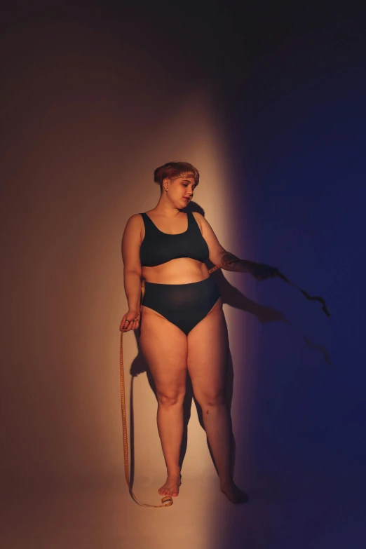 a woman in a black bikini holding a surfboard, an album cover, unsplash, renaissance, morbidly obese, holding a cane, standing in a dimly lit room, sport bra and dark blue shorts