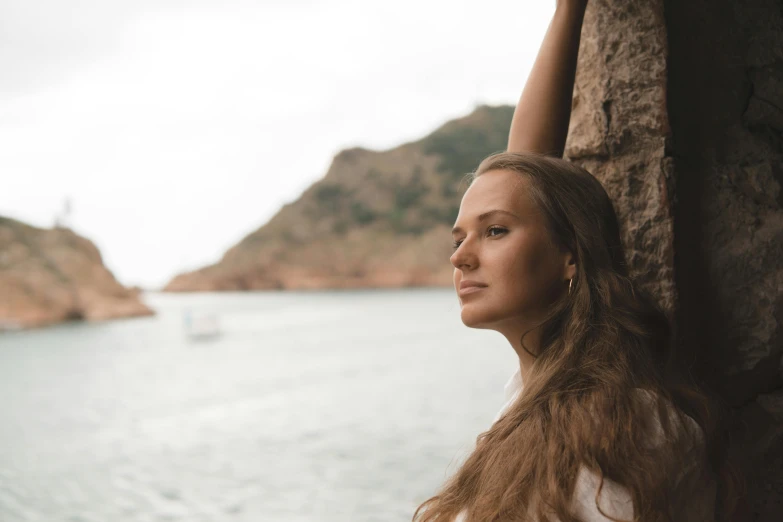 a woman leaning against a wall near a body of water, pexels contest winner, side portrait rugged girl, avatar image, looking off into the distance, young woman looking up