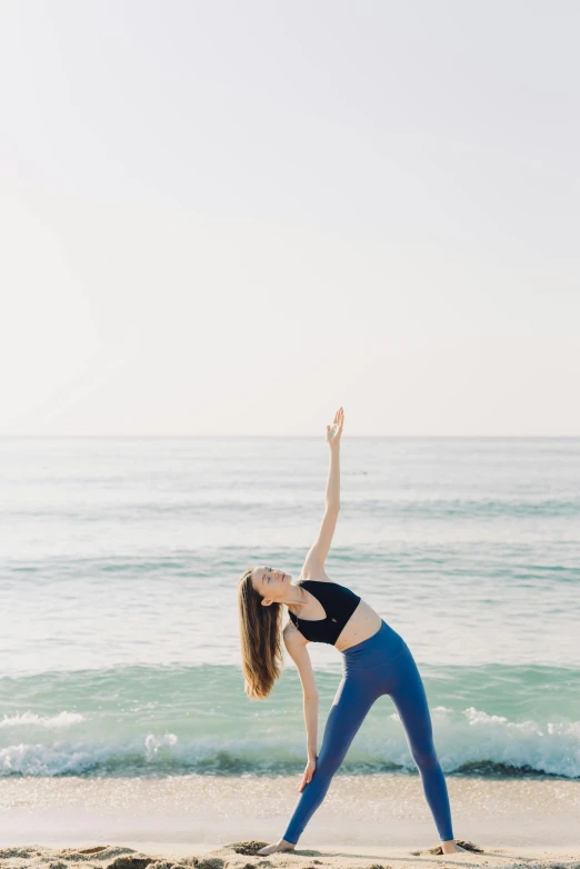 a woman doing a yoga pose on the beach, unsplash, arabesque, wave a hand at the camera, back arched, blue, side pose