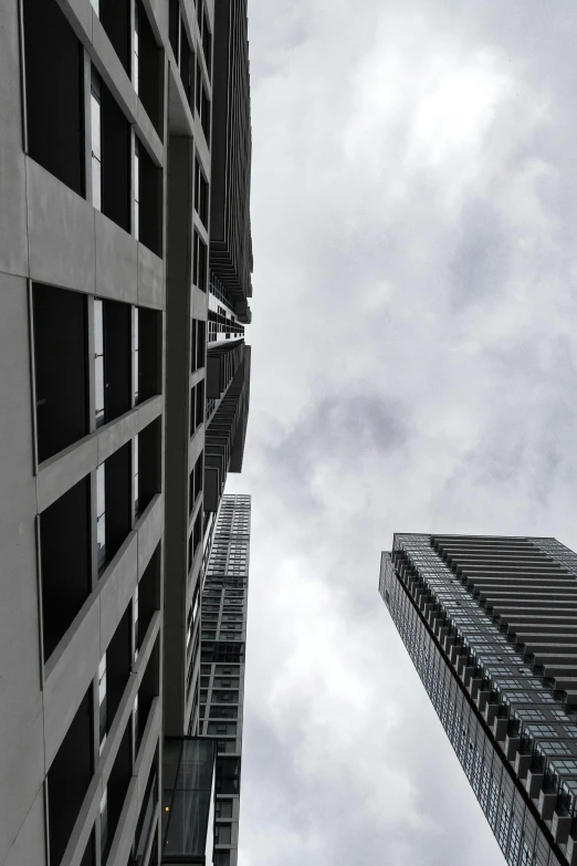 a couple of tall buildings next to each other, inspired by André Kertész, unsplash, gray skies, low quality photo, looking up, pov photo