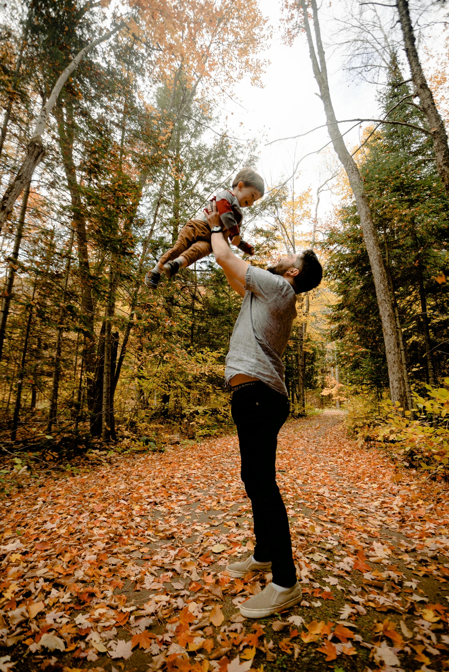 a man holding a child in his arms in the woods, pexels, vermont fall colors, flying shot, square, 8 k -