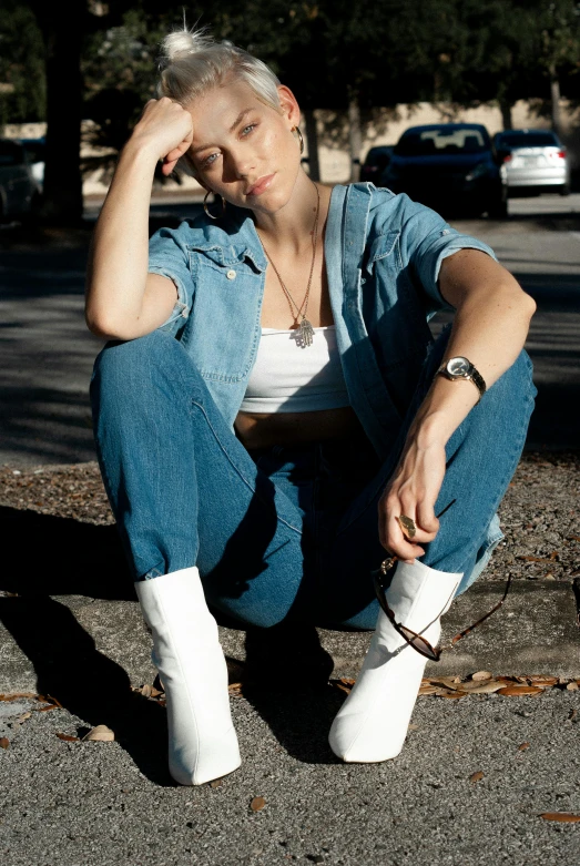 a woman sitting on the ground next to a fire hydrant, an album cover, by Sara Saftleven, trending on pexels, outfit : jeans and white vest, non binary model, cowgirl, thinking pose