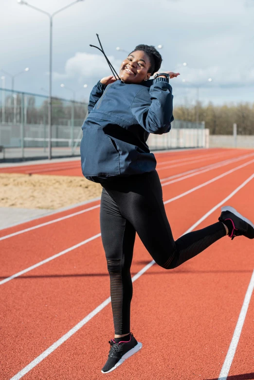 a woman in a blue jacket is running on a track, by Jan Tengnagel, unsplash, happening, doing a sassy pose, 15081959 21121991 01012000 4k, high arches, black