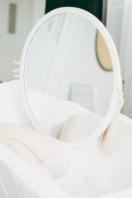 a woman laying on a bed in front of a mirror, pexels contest winner, aestheticism, soft white rubber, on a pale background, bathtub, round-cropped