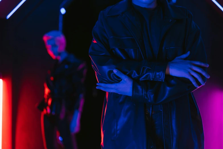 a man standing in a dark room with neon lights, an album cover, by Adam Marczyński, trending on pexels, realism, black leather garment, medium shot of two characters, light red and deep blue mood, concert