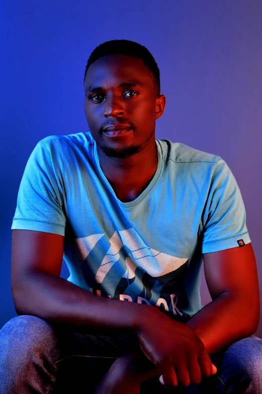a man sitting in front of a blue background, an album cover, by Chinwe Chukwuogo-Roy, pexels contest winner, standing with a black background, 15081959 21121991 01012000 4k, cute young man, glowing with colored light