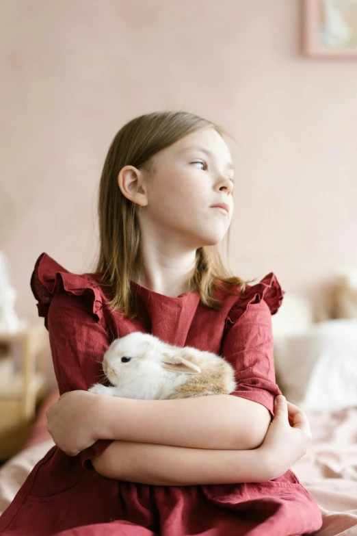 a little girl sitting on a bed holding a rabbit, inspired by Frieke Janssens, pexels contest winner, romanticism, arms folded, looking off into the distance, game, indoor scene