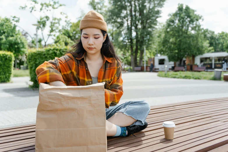 a woman sitting on a bench with a paper bag, trending on pexels, aboriginal australian hipster, over a dish and over a table, young asian girl, devastated