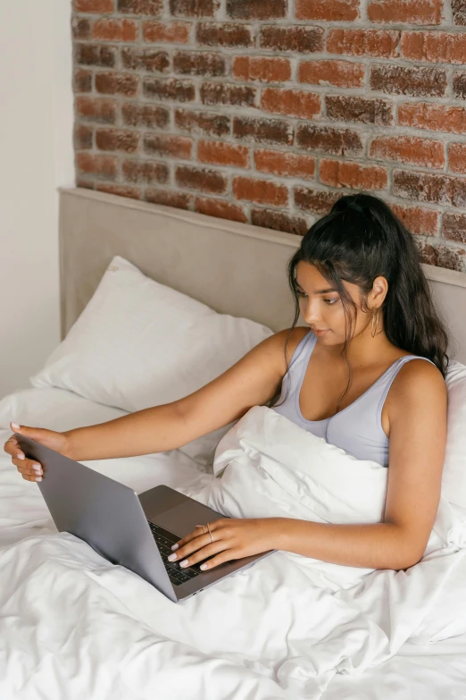 a woman laying in bed using a laptop computer, trending on pexels, happening, wearing a crop top, sleek design, bed on the right, indian girl with brown skin