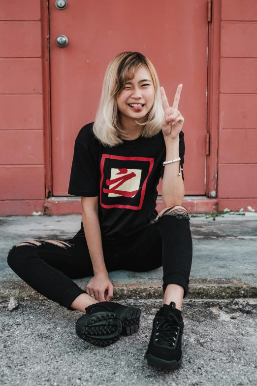 a woman sitting on the ground in front of a red door, a cartoon, inspired by Zhu Da, featured on instagram, graffiti, wearing a black!! t - shirt, peace sign, indonesia, discord profile picture