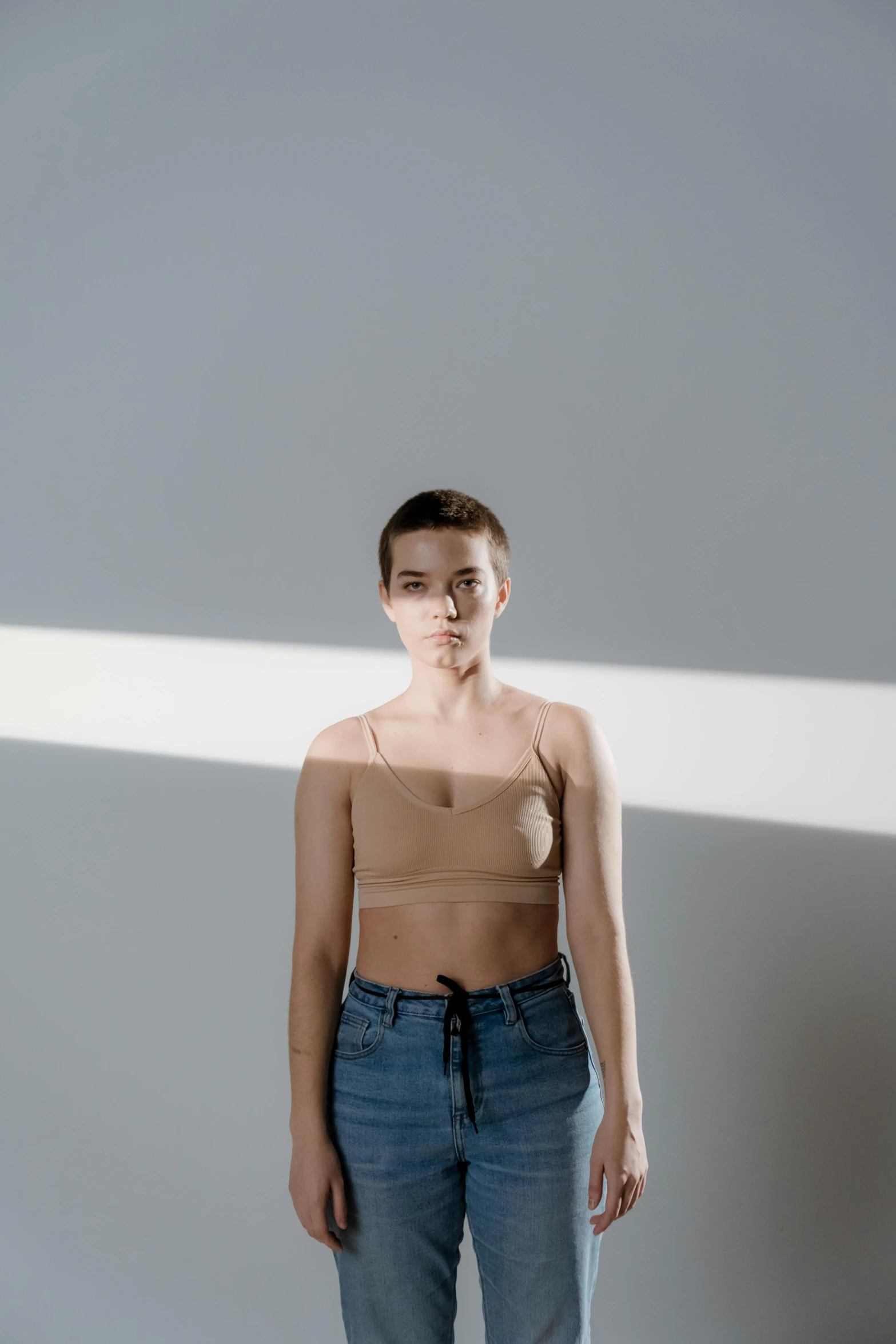 a woman standing in the middle of a room, inspired by Elsa Bleda, unsplash, minimalism, wearing crop top, sunlight filtering through skin, non binary model, plain background