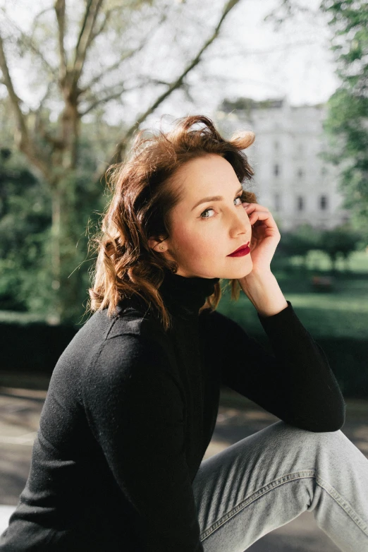 a woman sitting on a bench talking on a cell phone, a portrait, trending on unsplash, renaissance, camilla luddington, thoughtful pose, wearing turtleneck, with a park in the background