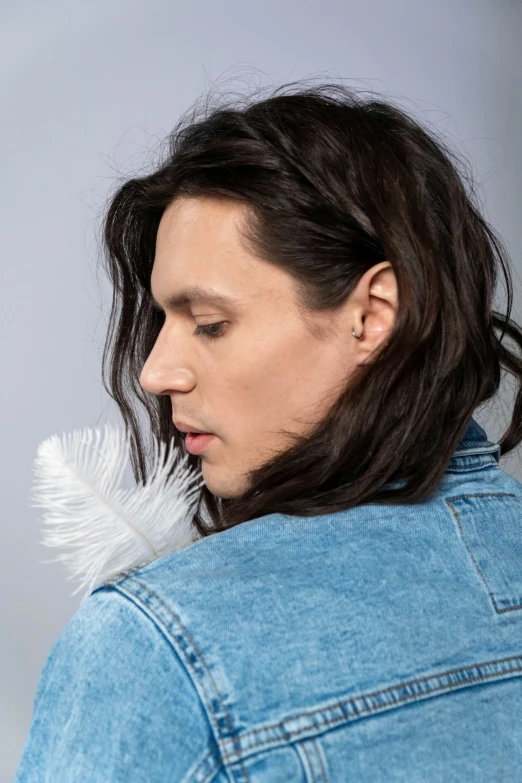 a man with long hair wearing a denim jacket, an album cover, inspired by Daniël Mijtens, trending on pexels, white feathers, close - up profile face, beautiful androgynous prince, portrait of tom holland