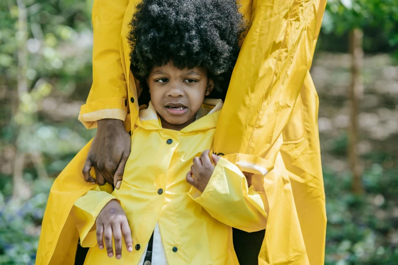 a woman standing next to a child in a yellow raincoat, pexels, afrofuturism, black man with afro hair, portrait of family of three, upset, closeup of an adorable