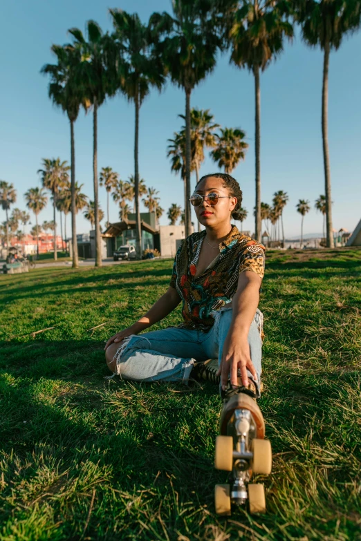 a man sitting in the grass with a skateboard, a portrait, by Winona Nelson, trending on unsplash, palm trees on the beach, girl wearing round glasses, the city of santa barbara, panoramic centered view of girl