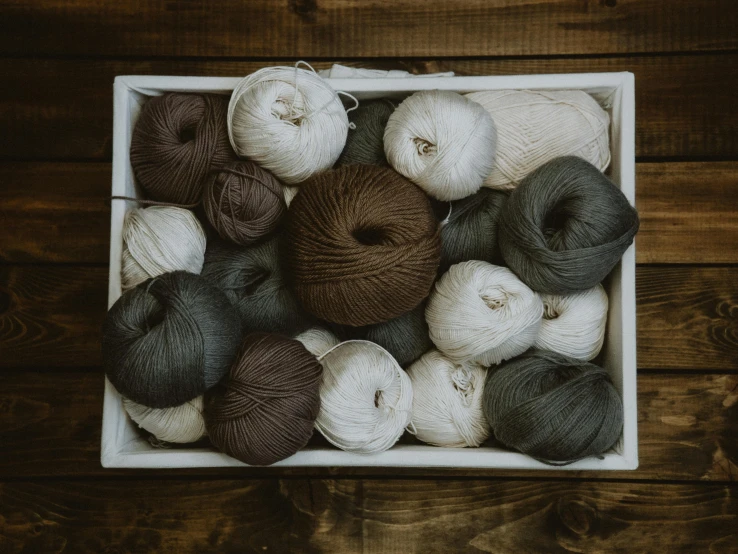 a box filled with balls of yarn on top of a wooden table, inspired by Eden Box, unsplash, renaissance, dark and white, taupe, group photo, linen