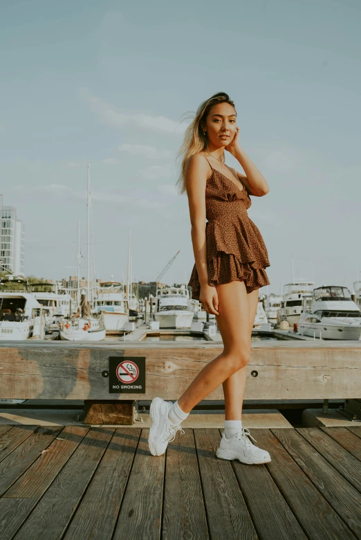 a woman standing on a dock talking on a cell phone, by Robbie Trevino, bra and shorts streetwear, in lace brown dress, docked at harbor, frill