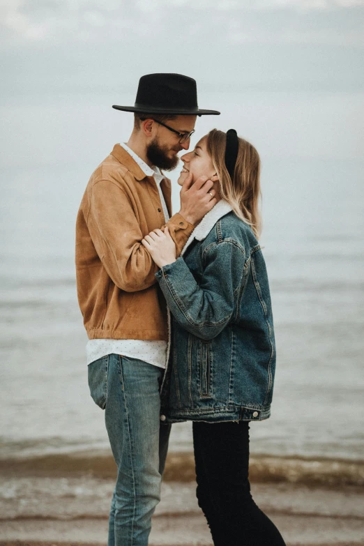 a man and woman kissing on the beach, a photo, by Matija Jama, trending on pexels, wearing a jeans jackets, orthodox, wearing a fedora, on grey background